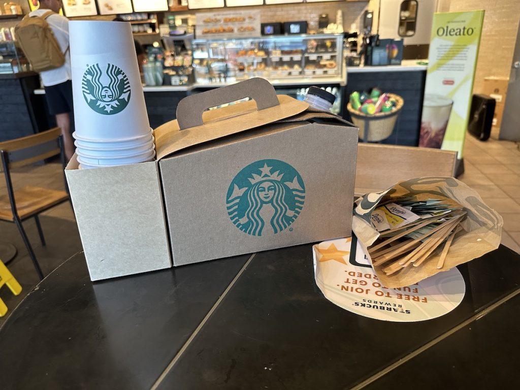 A loaded Starbucks traveler box of coffee and bag of sweeteners inside a Starbucks store
